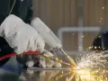 Ręce w rękawicach wykonują spawanie TIG, tworząc snop iskier na metalowej powierzchni.