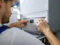 Serwisant reguluje nowoczesną instalację gazową w domu. Na wyświetlaczu kotła widoczna jest temperatura 30.0.
