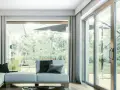 Nowoczesne okno tarasowe 3000x2300 cena. Jasny salon z widokiem na ogród, wygodna sofa i zasłony.
