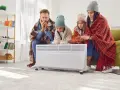 Rodzina otulona kocami grzeje ręce przy grzejniku, czekając, aż zacznie się sezon grzewczy.