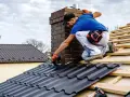 Dachówka w trakcie montażu, pracownik przy kominie. Sprawdź aktualną cenę robocizny dachu za m2.