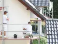 Dwóch malarzy na rusztowaniu maluje elewację. Szukają najlepszej farby elewacyjnej na forum, by dom wyglądał jak nowy.