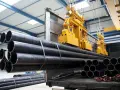 Żółte suwnice podnoszą stalowe rury w hali produkcyjnej. Budowa suwnicy jest kluczowa dla sprawnego transportu materiałów.