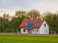 Nowoczesny dom energooszczędny z panelami słonecznymi na dachu, otoczony zielenią.