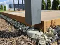 Solidny, podwyższony taras na gruncie, oparty na betonowych stopach i kamieniach. Drewniana konstrukcja z ciemnym słupem.