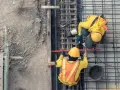 Dwóch budowlańców w żółtych kamizelkach pracuje przy zbrojeniu. To kluczowy etap w budowie każdego obiektu budowlanego.