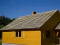 Budowa domu z żółtej deski. Na dachu układana jest papa, przygotowana pod pokrycie.