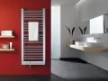 Nowoczesna łazienka z czerwonymi ścianami. Grzejnik z podłączeniem od dołu, z białym ręcznikiem. Obok dwie umywalki nablatowe.