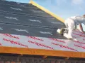 Pracownik montuje ocieplenie nakrokwiowe na dachu, układając warstwy izolacji i membrany.