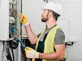 Elektryk w kasku i kamizelce odblaskowej pracuje przy skrzynce z przewodami. Dokładna wycena koszt instalacji elektrycznej.