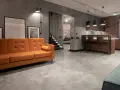 Nowoczesny salon z pomarańczową kanapą i kuchnią w stylu industrialnym. Podłoga z mikrocementu, cena za m2 tej powierzchni jest atrakcyjna.