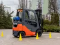 Pomarańczowo-szary wózek widłowy Toyota z butlą gazową, otoczony żółtymi pachołkami, gotowy do testów UDT.
