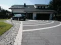 Nowoczesny dom z garażem, przed którym rozciąga się efektowny beton na podjazd, ozdobiony białymi pasami tworzącymi łuki.