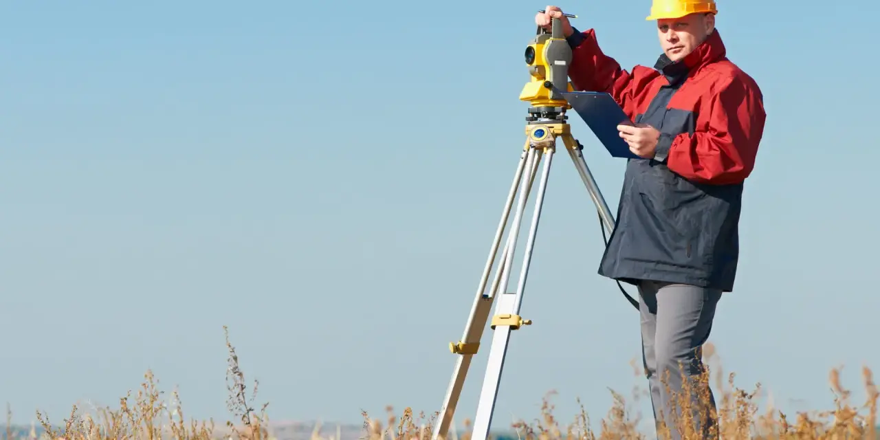 Geodeta w żółtym kasku pracuje z tachimetrem na polu. Zastanawiasz się, ile kosztuje geodeta?