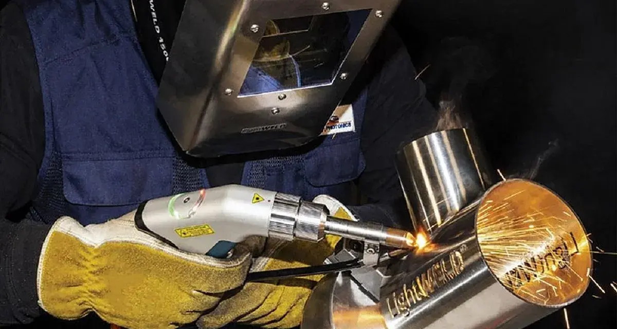 Operator w masce spawalniczej wykonuje napawanie laserowe metalowych elementów, tworząc iskrzące spoiny.