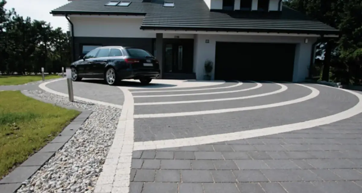Nowoczesny dom z garażem, przed którym rozciąga się efektowny beton na podjazd, ozdobiony białymi pasami tworzącymi łuki.