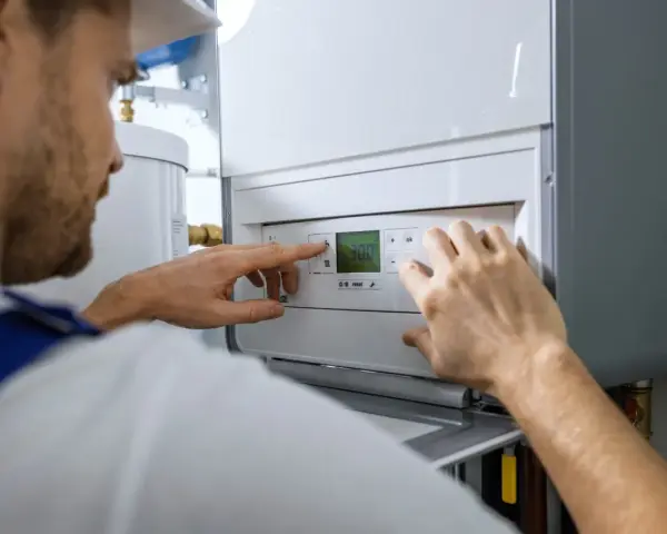 Serwisant reguluje nowoczesną instalację gazową w domu. Na wyświetlaczu kotła widoczna jest temperatura 30.0.