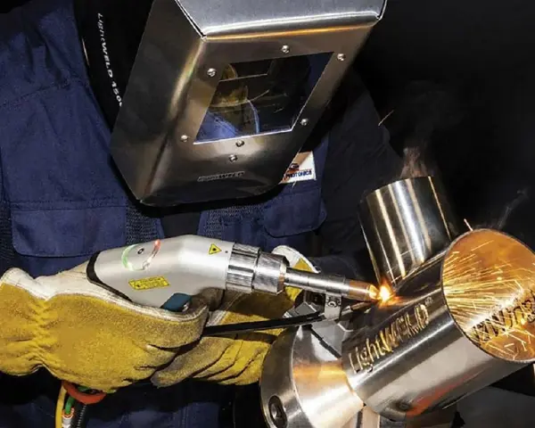 Operator w masce spawalniczej wykonuje napawanie laserowe metalowych elementów, tworząc iskrzące spoiny.