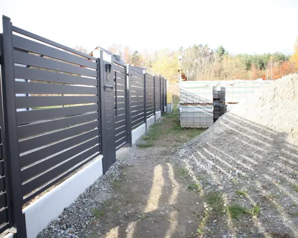 Solidny fundament pod bramę przesuwną, gotowy na montaż nowoczesnego ogrodzenia. Obok materiały budowlane.