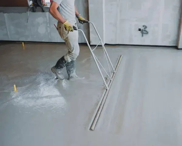Pracownik wyrównuje świeżą wylewkę betonową. Czas, ile schnie wylewka betonowa, zależy od wielu czynników.