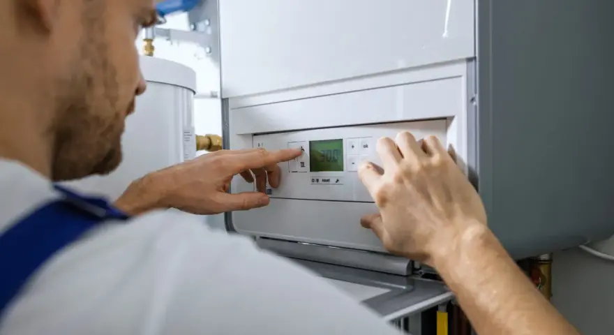 Serwisant reguluje nowoczesną instalację gazową w domu. Na wyświetlaczu kotła widoczna jest temperatura 30.0.