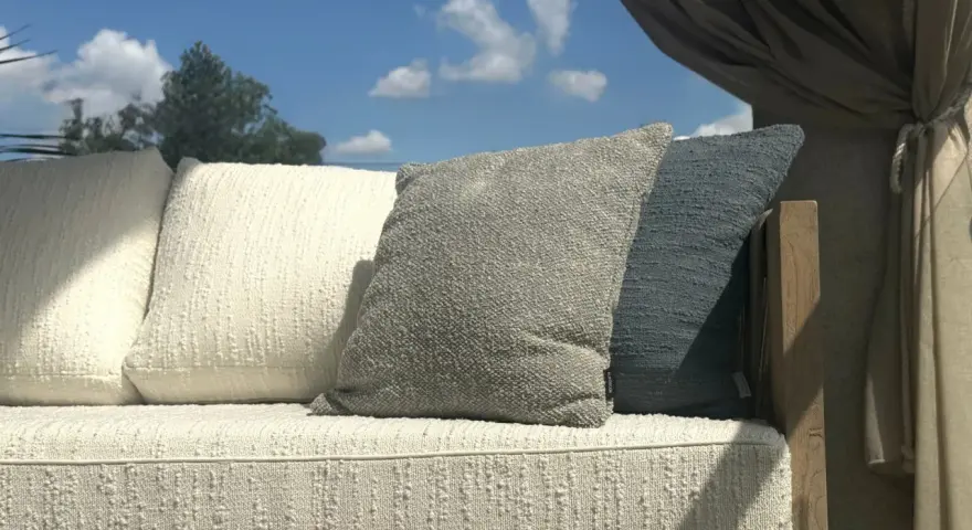 Wygodna sofa z poduszkami, osłonięta zasłonami, stoi na tle błękitnego nieba. Jej rama wykonana jest z pięknego, naturalnego **drewna tekowego**.