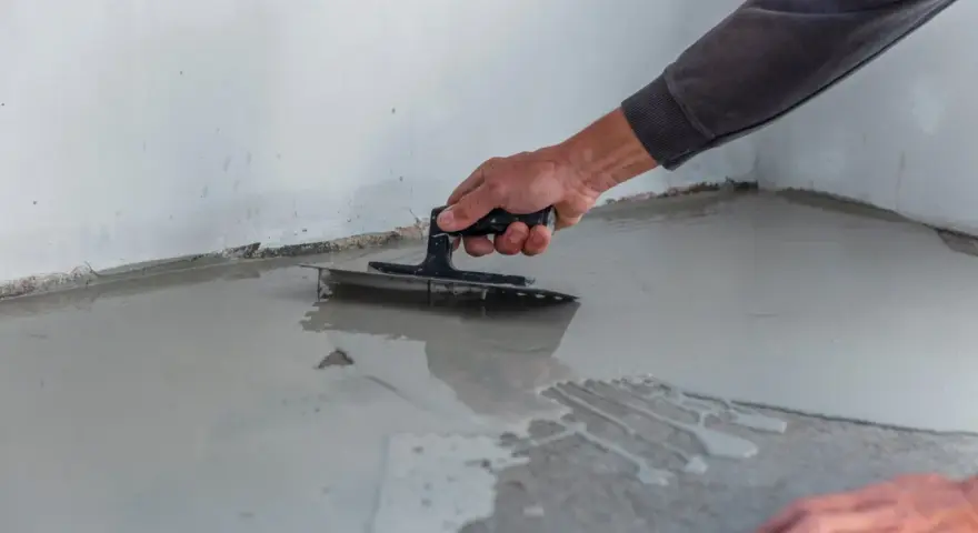Ręka rozprowadza masę samopoziomującą po podłodze. Czas, ile schnie wylewka samopoziomująca, zależy od warunków.