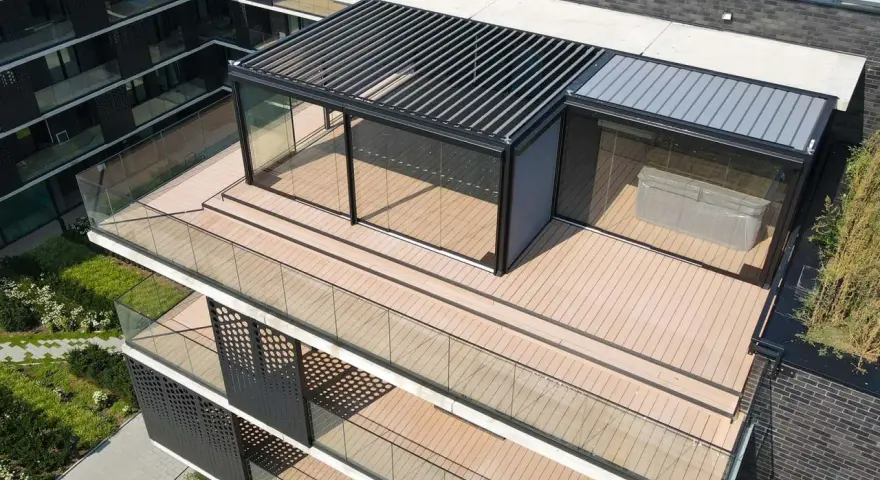 Nowoczesny taras na dachu z przeszklonym pawilonem i pergolą. Drewniana podłoga i szklane balustrady tworzą elegancką przestrzeń.