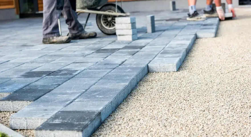 Układanie nowoczesnych płyt betonowych, co zamiast kostki brukowej. Pracownicy z taczką tworzą ścieżkę.